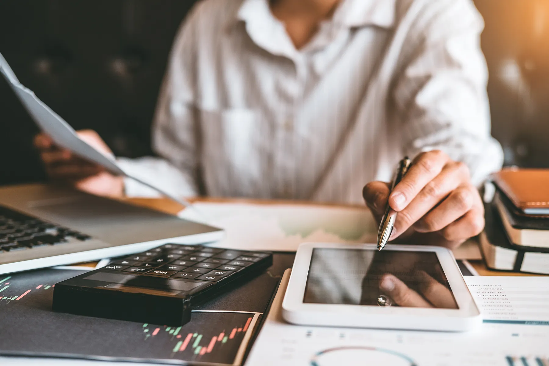 Profissional analisando documentos e gráficos em tablet e calculadora durante gestão financeira empresarial.