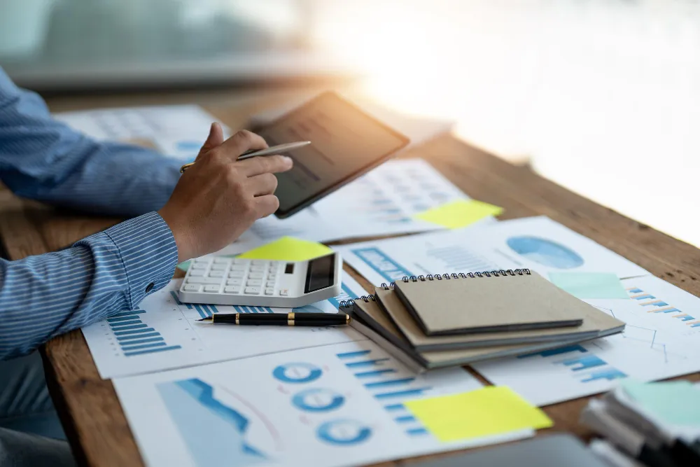 Planejamento financeiro pessoal: o que é, benefícios, quando e como fazer Pessoa analisando gráficos financeiros com tablet e calculadora, ilustrando práticas essenciais de planejamento financeiro pessoal.