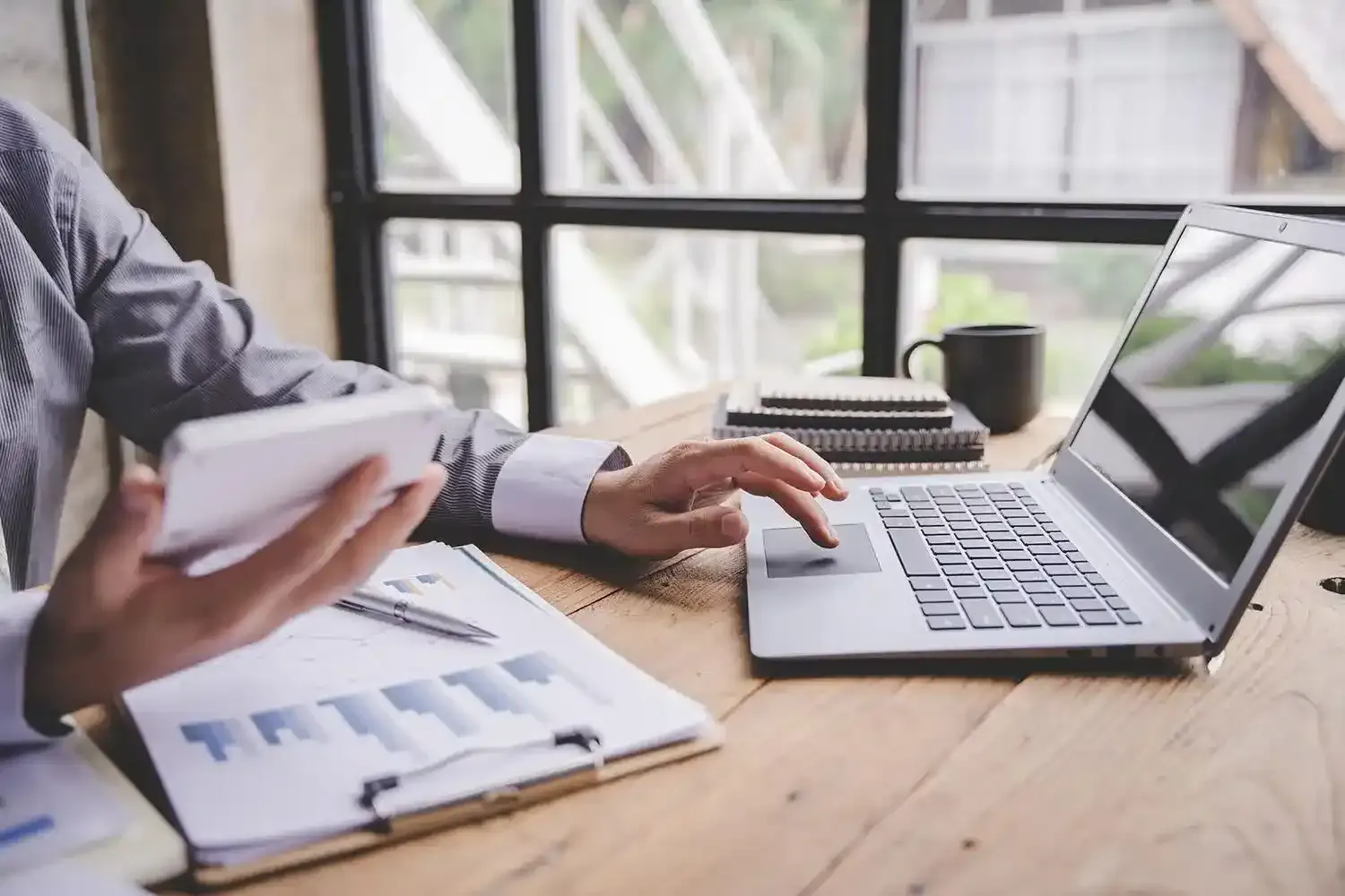 Pessoa analisando documentos financeiros e computador em mesa de trabalho, representando planejamento sucessório e organização patrimonial