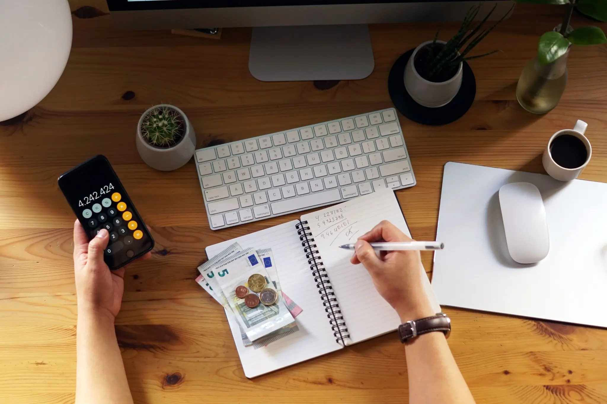 Orçamento financeiro: o que é, para que serve, quando e como fazer Pessoa organizando orçamento financeiro com calculadora, anotações, dinheiro em espécie e computador sobre mesa de trabalho.