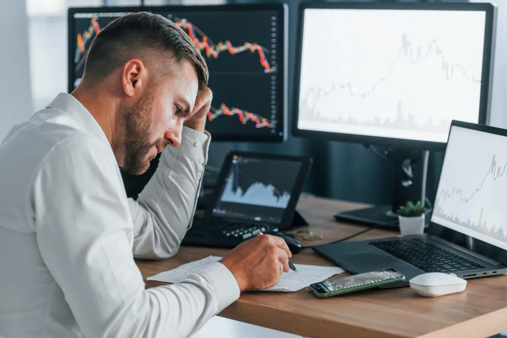 Riscos financeiros: o que são, tipos e 5 práticas de FP&A para mitigação em grandes empresas Riscos financeiros ilustrados por profissional analisando gráficos de investimentos com preocupação em escritório