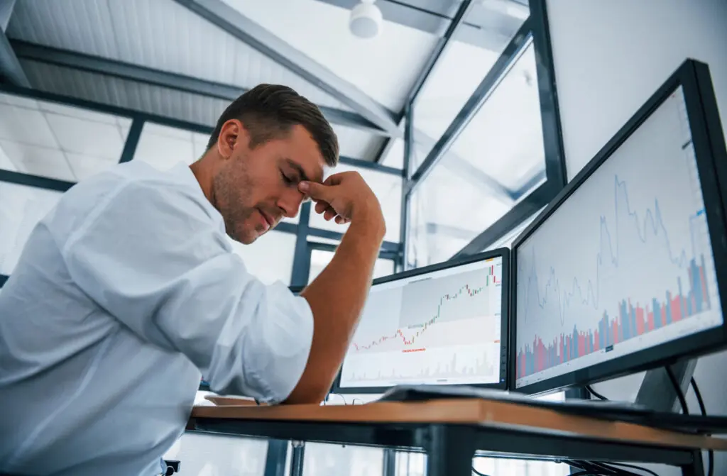 Profissional estressado diante de monitores com gráficos financeiros representando riscos no controle financeiro empresarial