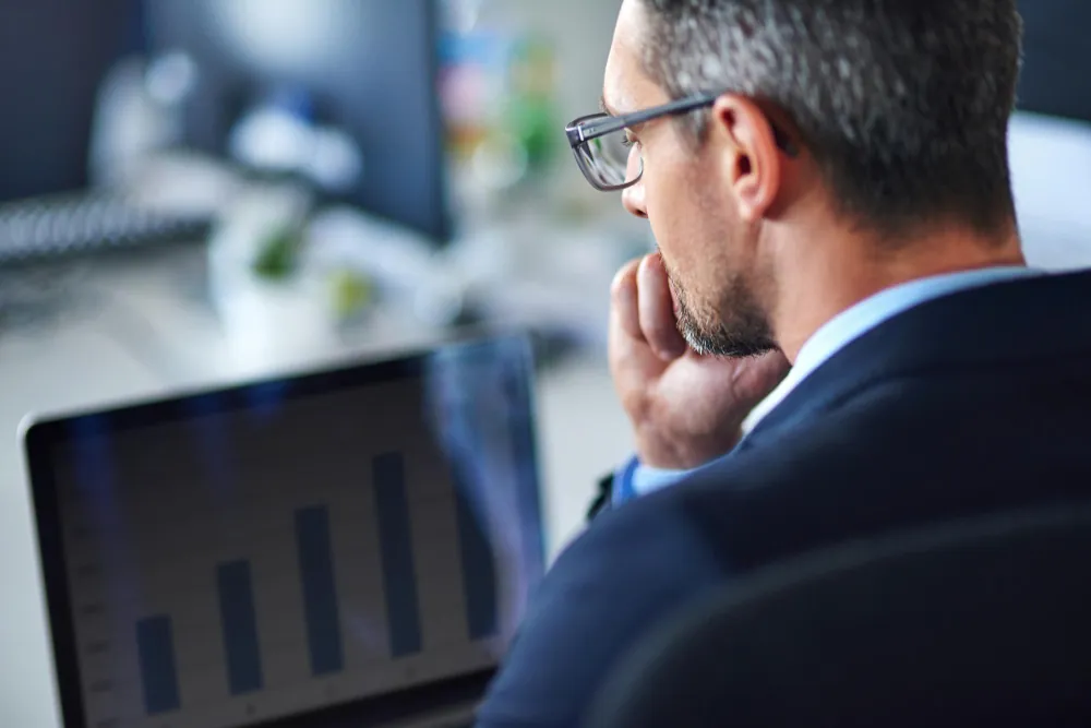 Ponto de equilíbrio: o que é, tipos, como calcular e por que toda empresa precisa saber o seu Homem de terno analisando gráfico de barras em notebook, refletindo sobre o ponto de equilíbrio do negócio